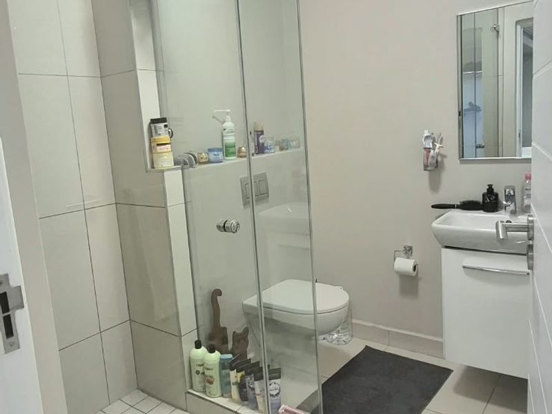 Modern bathroom featuring a glass-enclosed shower, wall-mounted toilet, and a sleek vanity basin with neutral floor and wall tiling.