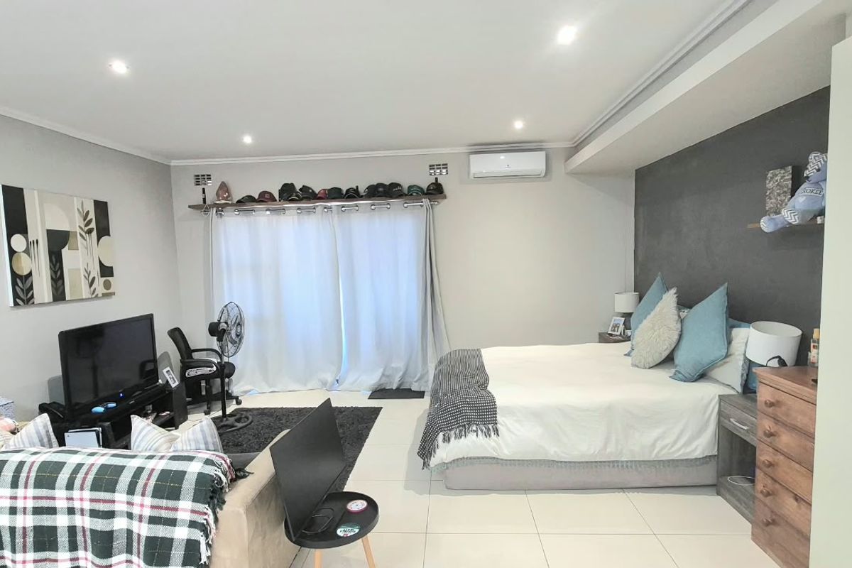 Spacious bedroom featuring tiled flooring, recessed downlighting, a split-system air conditioner, and a built-in wardrobe with a modern feature wall.