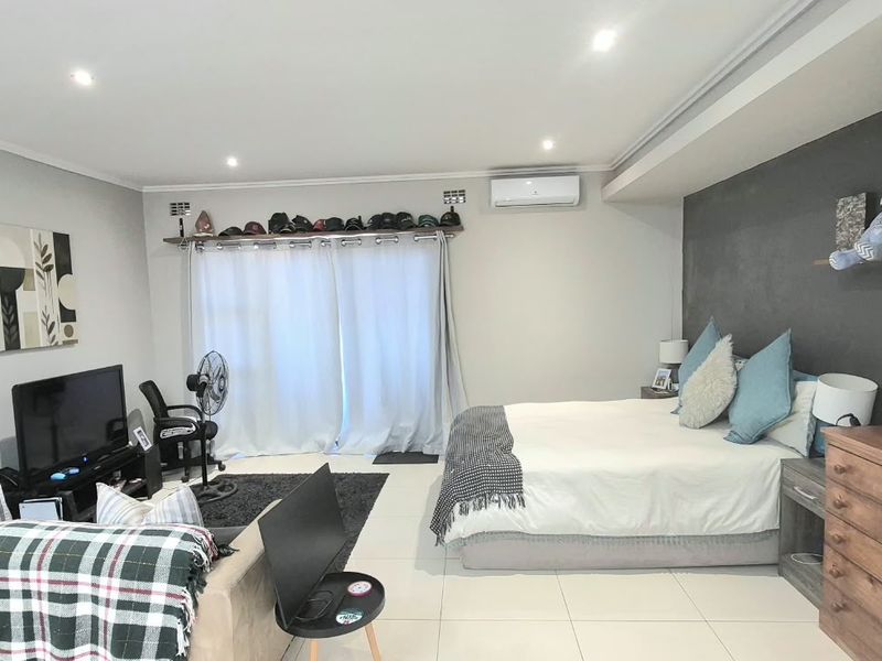 Spacious bedroom featuring tiled flooring, recessed downlighting, a split-system air conditioner, and a built-in wardrobe with a modern feature wall.