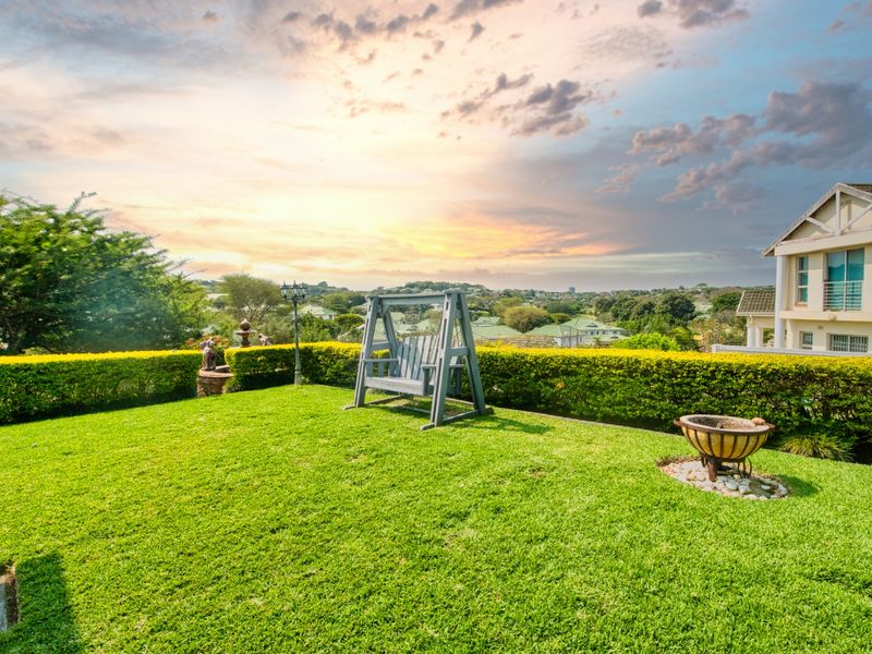 A well-maintained garden area featuring manicured hedges, lush lawn, and scenic elevated views of the surrounding neighborhood.