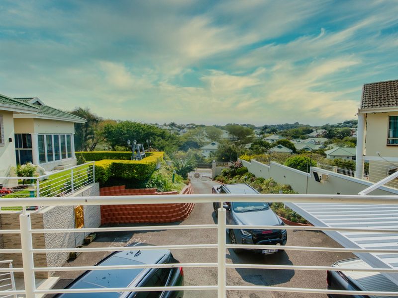 Elevated view from a balcony overlooking the driveway, landscaped garden, and surrounding residential neighborhood.