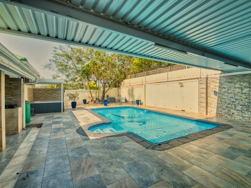 A spacious outdoor pool area featuring a covered patio with tiled flooring, stone-clad feature walls, and a secure swimming pool.