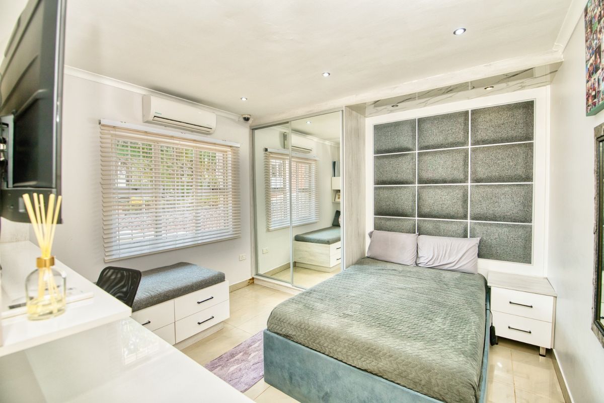 Modern bedroom featuring built-in mirrored wardrobes, a custom upholstered headboard wall, split-system air conditioning, and tiled flooring with recessed lighting.