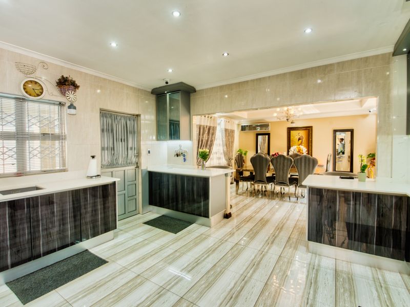 Modern open-plan kitchen and dining area featuring sleek cabinetry, stone countertops, and polished tiled flooring with recessed lighting throughout.