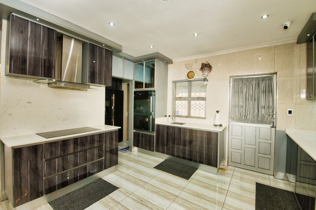 Modern kitchen featuring dark wood-grain cabinetry, stone countertops, integrated appliances, and tiled flooring with recessed ceiling lighting.