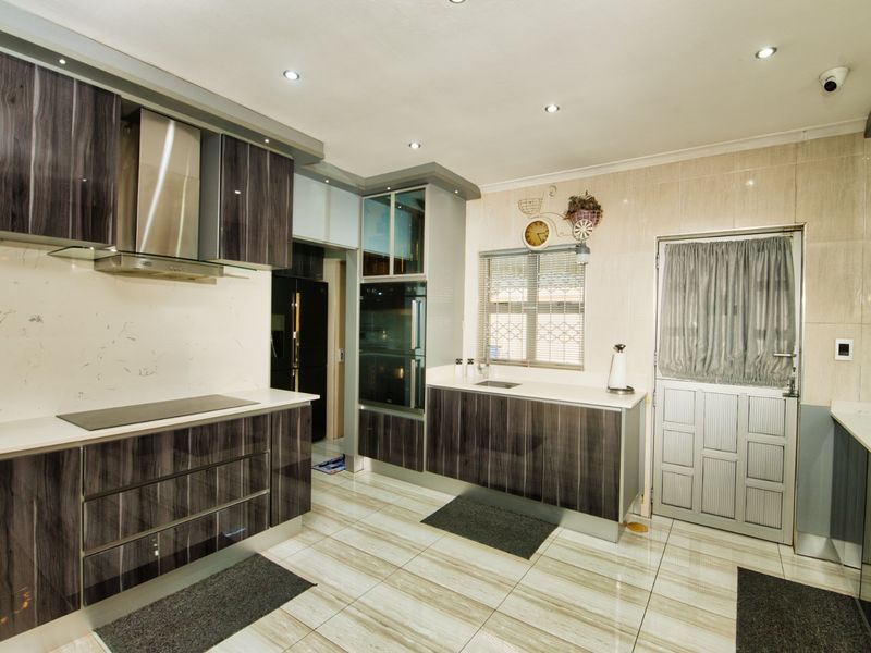 Modern kitchen featuring dark wood-grain cabinetry, stone countertops, integrated appliances, and tiled flooring with recessed ceiling lighting.