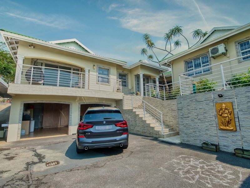 Front elevation of a multi-level house featuring a double garage, stone-clad retaining wall, external staircase, and an upper-level balcony with metal railings.