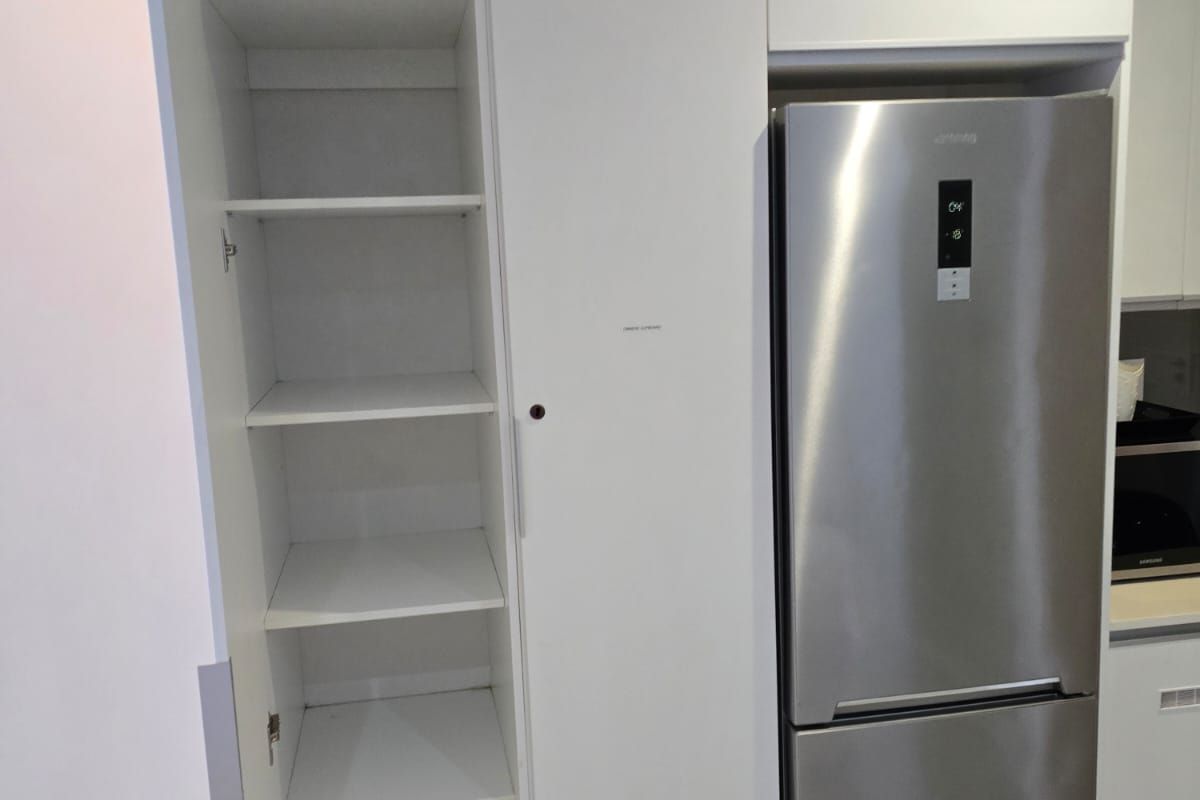 A modern kitchen featuring clean white built-in pantry cabinetry with integrated shelving and a dedicated space for a refrigerator.