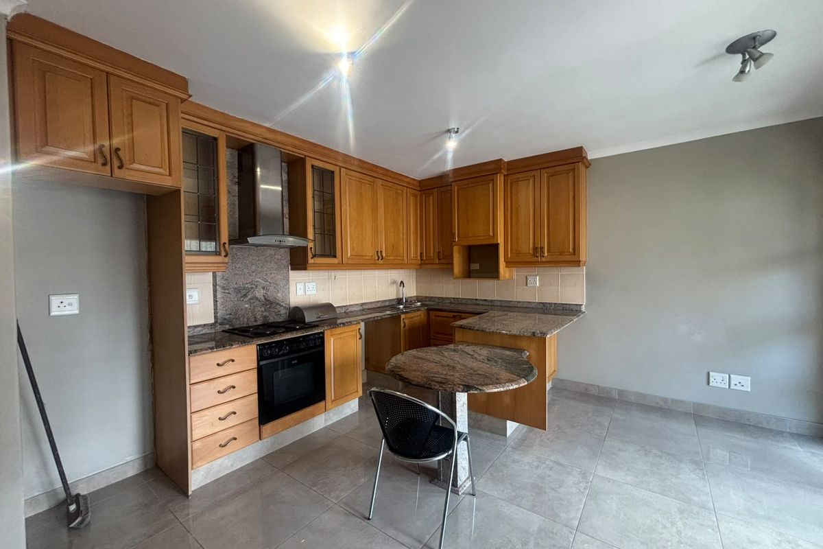 A functional kitchen featuring wooden cabinetry, granite countertops, built-in oven, hob, and tiled flooring, offering a practical layout for daily cooking.