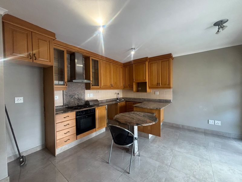 A functional kitchen featuring wooden cabinetry, granite countertops, built-in oven, hob, and tiled flooring, offering a practical layout for daily cooking.