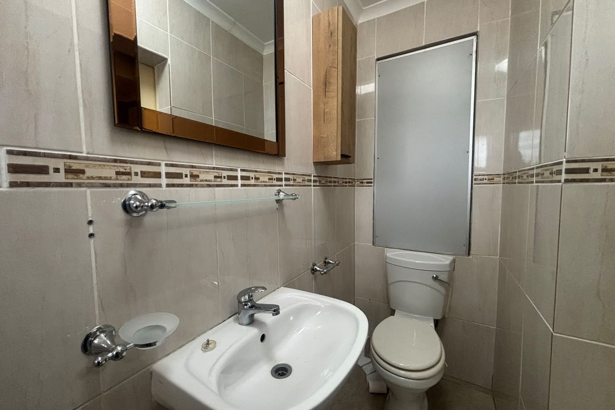 A compact bathroom featuring tiled walls, a pedestal basin with chrome mixer tap, a toilet, and a wall-mounted mirror and cabinet.