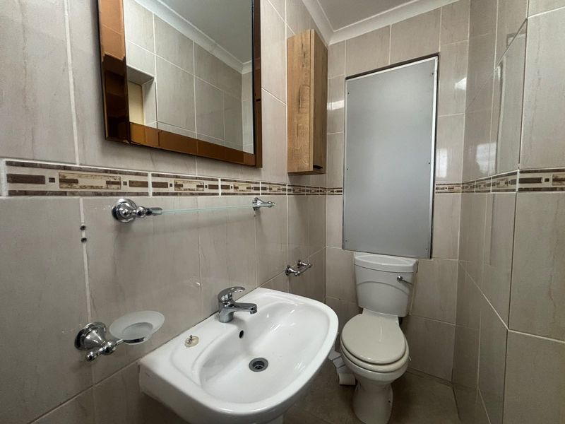 A compact bathroom featuring tiled walls, a pedestal basin with chrome mixer tap, a toilet, and a wall-mounted mirror and cabinet.
