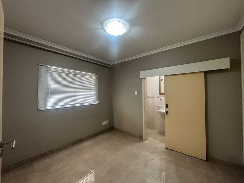 An empty bedroom featuring tiled flooring, neutral wall paint, a sliding door leading to an en-suite bathroom, and venetian blinds.