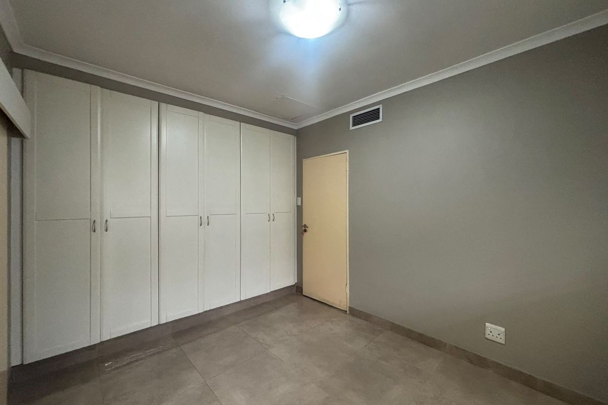 A clean, empty bedroom featuring neutral grey walls, tiled flooring, and extensive built-in cupboard storage.