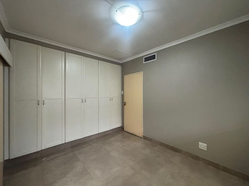 A clean, empty bedroom featuring neutral grey walls, tiled flooring, and extensive built-in cupboard storage.