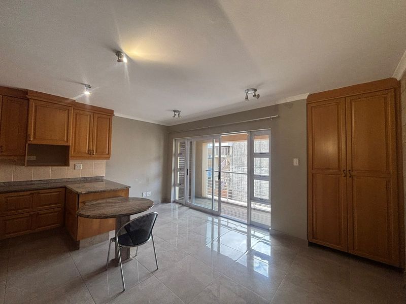 Open-plan living area featuring a kitchen with wooden cabinetry, granite countertops, tiled floors, and a sliding door leading to a balcony.