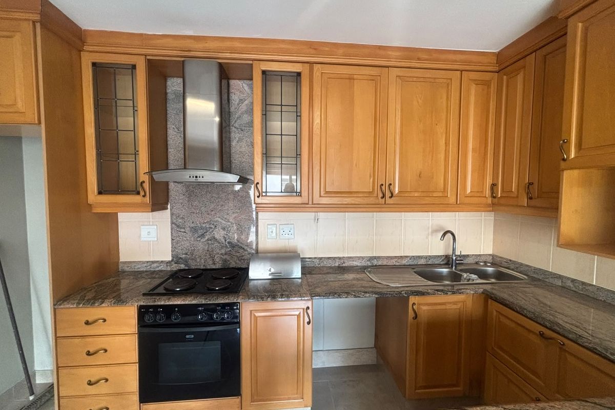 A functional kitchen featuring wooden cabinetry, granite countertops, a built-in oven with hob, and a stainless steel extractor fan.