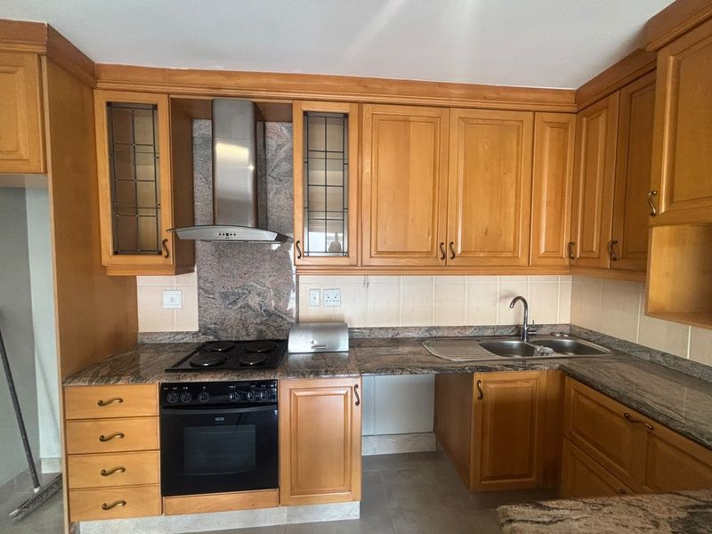 A functional kitchen featuring wooden cabinetry, granite countertops, a built-in oven with hob, and a stainless steel extractor fan.