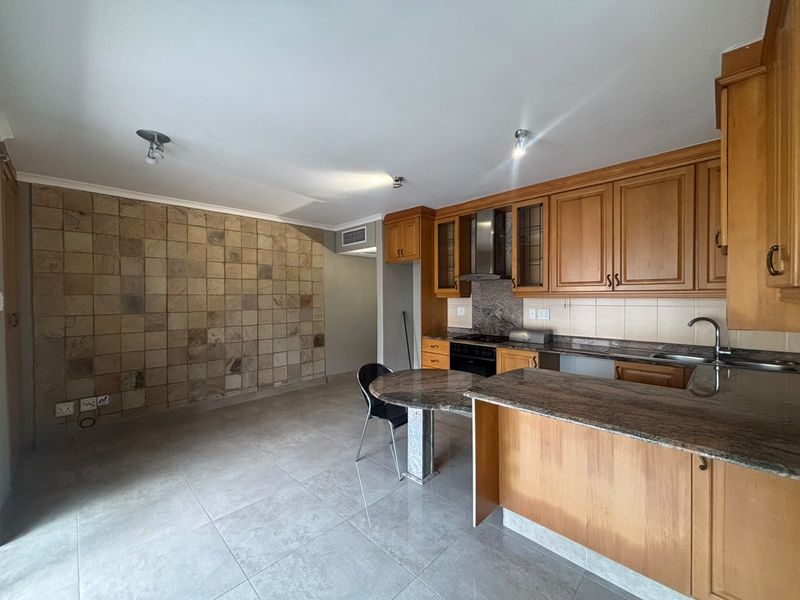 Kitchen featuring wooden cabinetry, granite countertops, built-in oven, extractor fan, and a distinctive stone tile feature wall with tiled flooring.