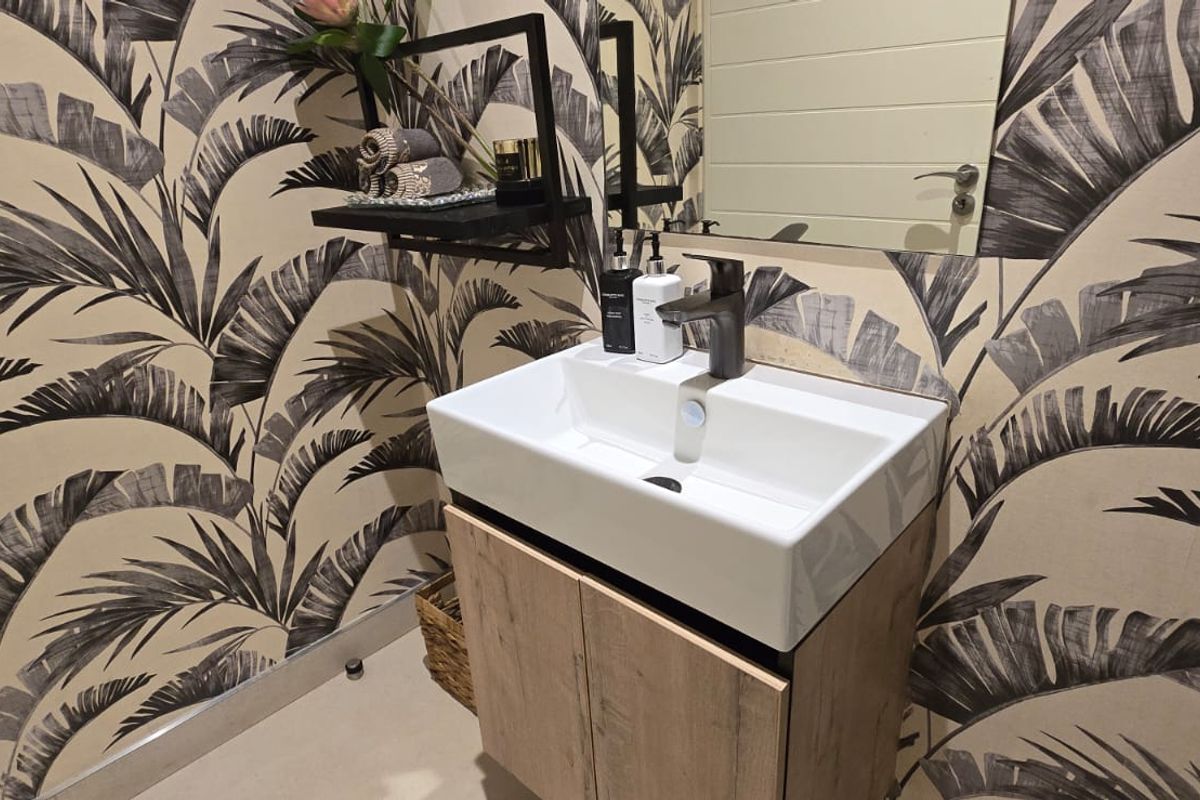 A modern bathroom featuring a contemporary vanity cabinet with a ceramic basin, mixer tap, and stylish palm-leaf patterned wallpaper.