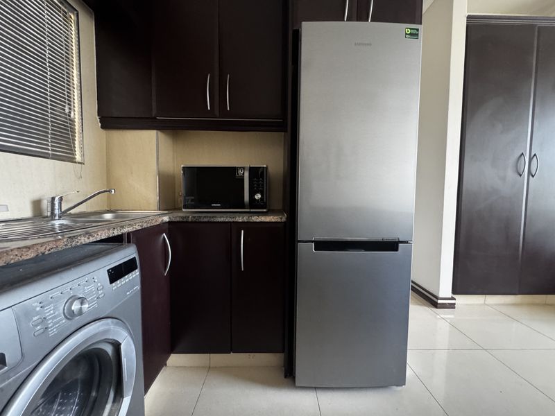 A functional kitchen featuring dark wood cabinetry, granite countertops, stainless steel sink, and tiled flooring, providing a practical and compact cooking space.
