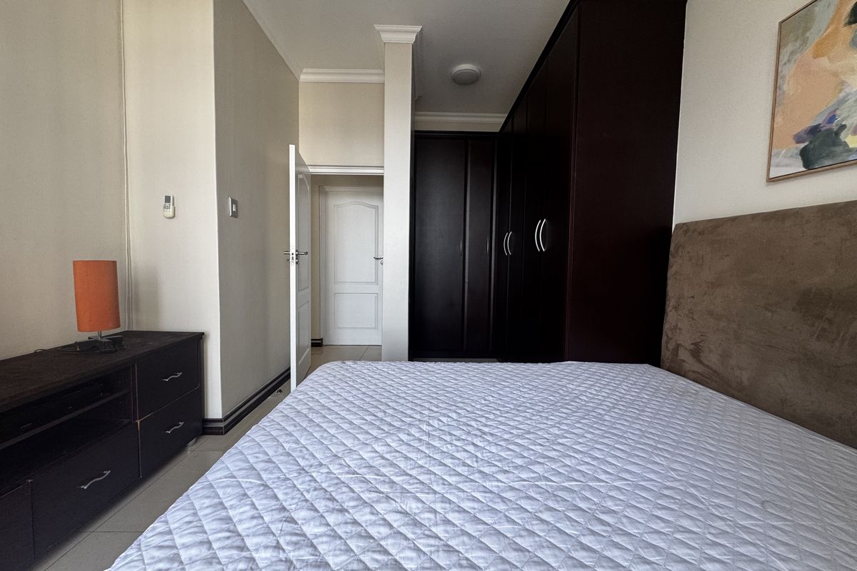 A well-maintained bedroom featuring dark wood built-in cupboards, neutral wall finishes, and tiled flooring, providing a clean and functional living space.