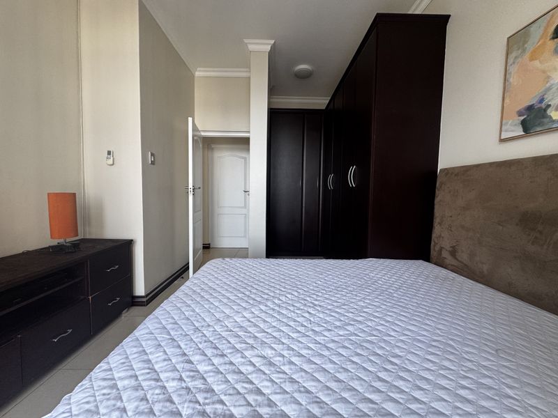 A well-maintained bedroom featuring dark wood built-in cupboards, neutral wall finishes, and tiled flooring, providing a clean and functional living space.