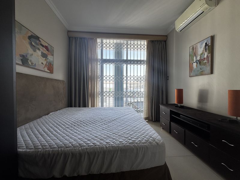 A well-maintained bedroom featuring tiled flooring, a wall-mounted split-system air conditioner, and a secure metal gate over the window.
