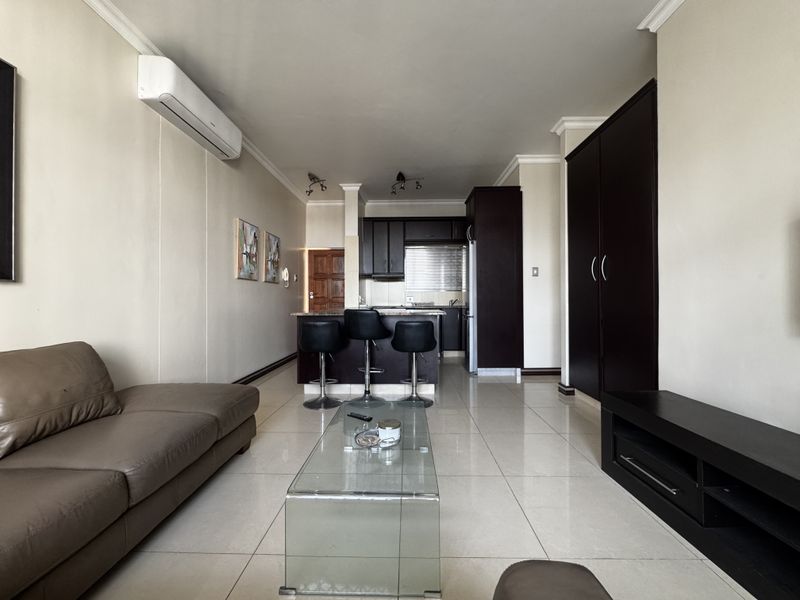 Open-plan living area featuring tiled floors, a split-system air conditioner, and a compact kitchen with built-in cabinetry and an island.