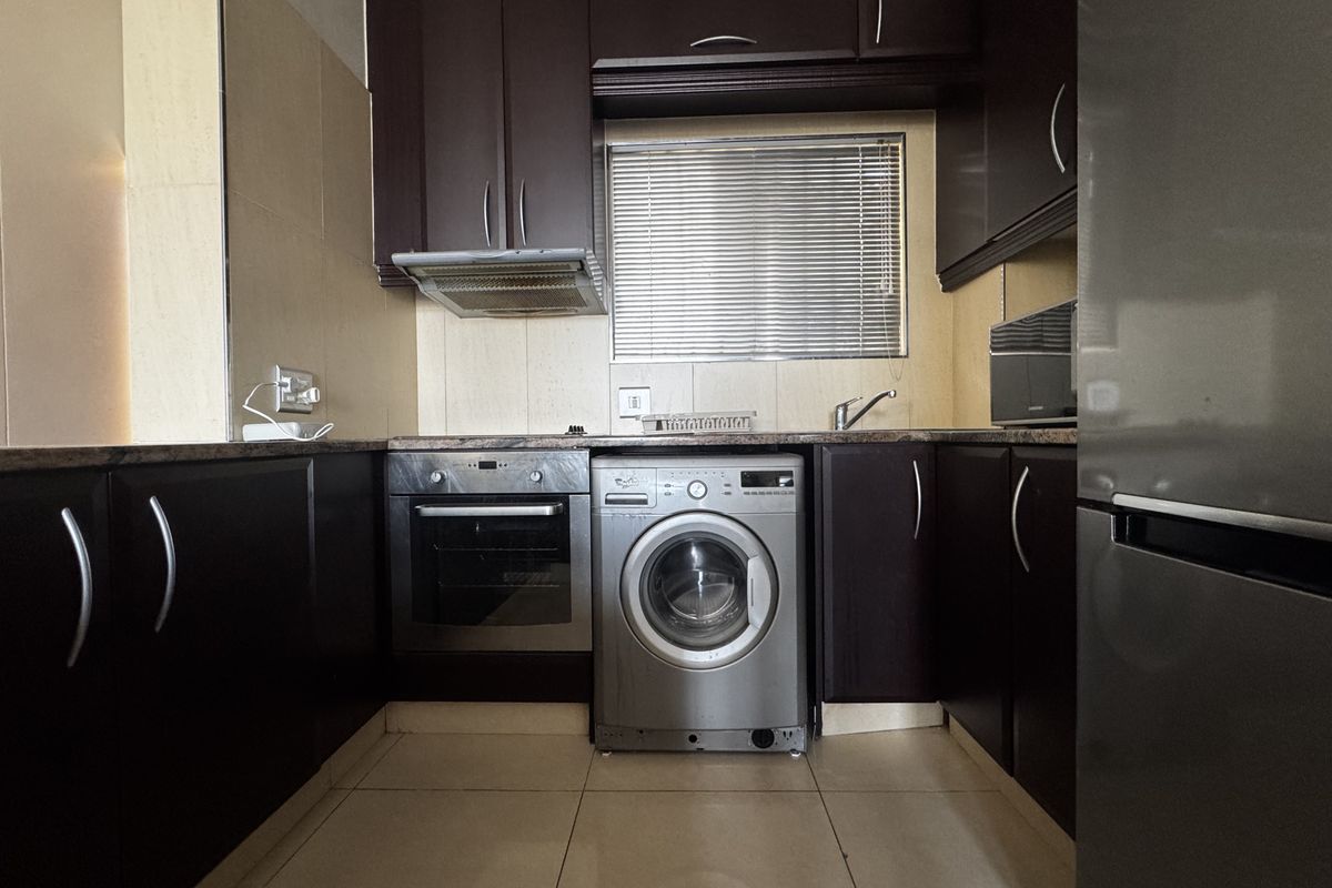 Compact kitchen featuring dark wood cabinetry, granite countertops, built-in oven, extractor fan, and integrated laundry appliance space.
