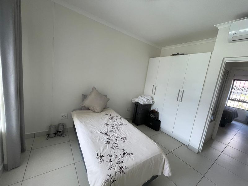 A clean bedroom featuring tiled flooring, a built-in wardrobe, and a wall-mounted air conditioning unit.