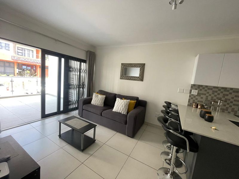 Modern open-plan living area featuring tiled floors, a sleek kitchen with stone countertops, and a sliding door leading to a private balcony.