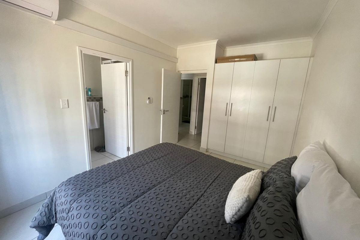 A well-maintained bedroom featuring built-in cupboards, tiled flooring, and an integrated air conditioning unit, with direct access to an en-suite bathroom.
