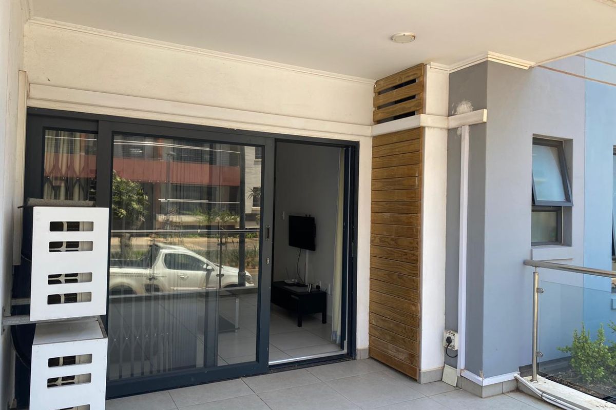 A covered balcony featuring tiled flooring, a glass balustrade, and a decorative timber slat panel, providing seamless access to the interior living space.