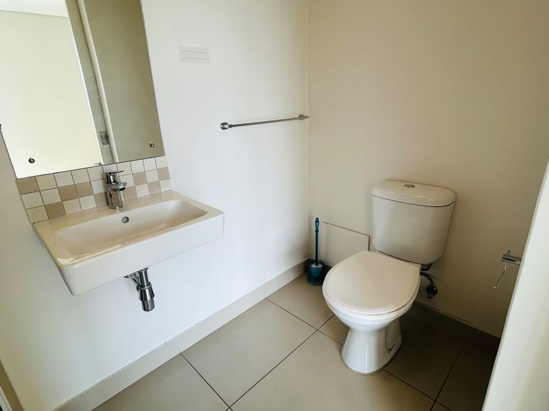 A clean and functional guest bathroom featuring a wall-mounted basin, modern toilet, and neutral ceramic floor tiling.