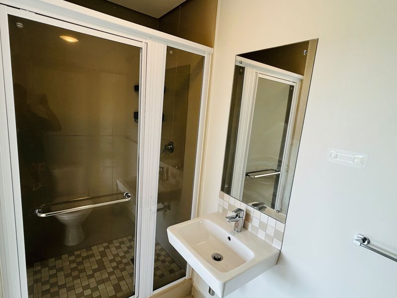 A functional bathroom featuring a shower enclosure with tiled flooring, a wall-mounted basin with a mixer tap, and a wall mirror.