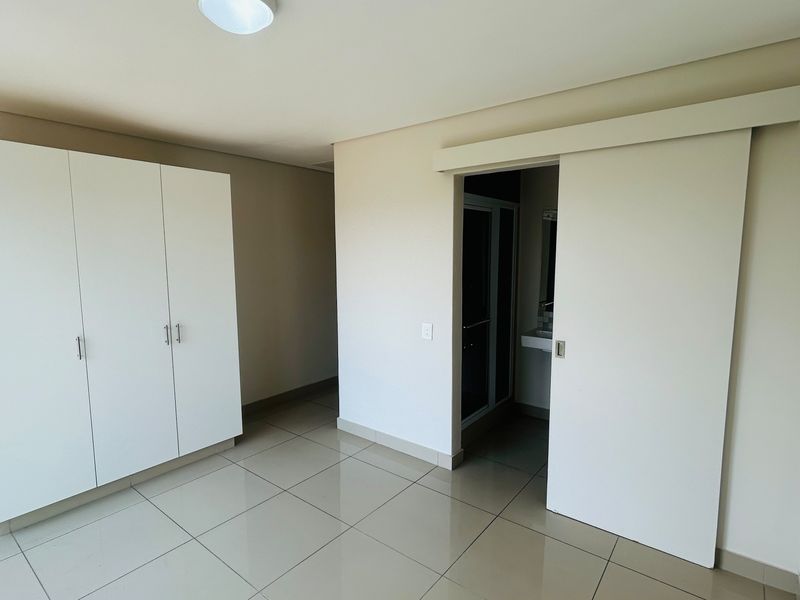 A clean, empty bedroom featuring neutral tiled flooring, a built-in wardrobe, and a sliding door leading to an en-suite bathroom.