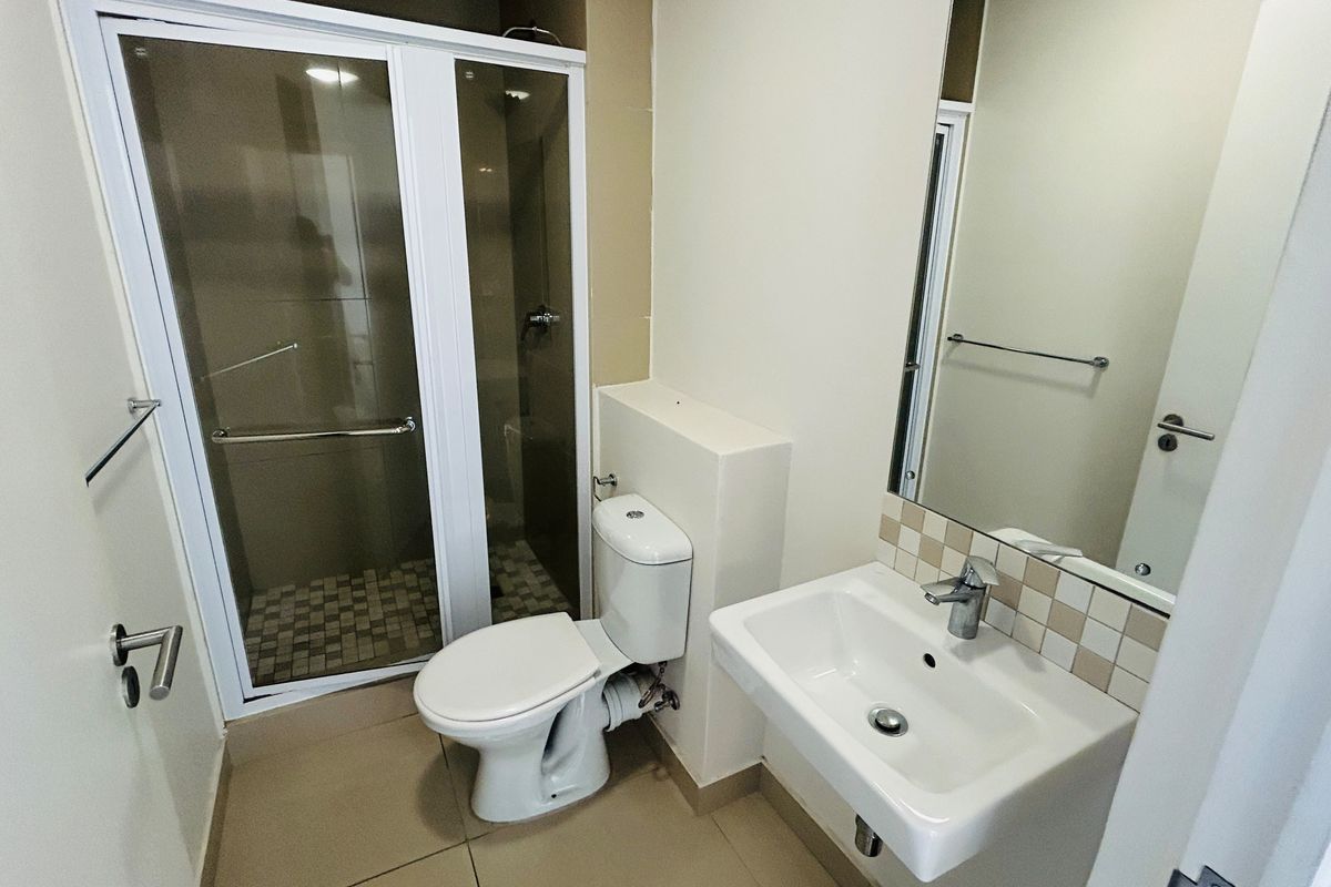 A clean, functional bathroom featuring a glass-enclosed shower, a wall-mounted basin with tiled splashback, and neutral floor tiling.