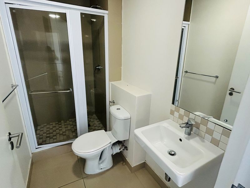 A clean, functional bathroom featuring a glass-enclosed shower, a wall-mounted basin with tiled splashback, and neutral floor tiling.