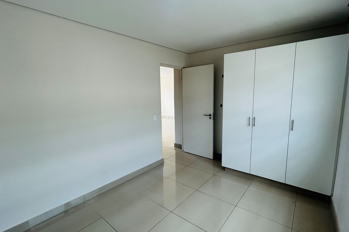 A bright, empty bedroom featuring neutral tiled flooring and a clean, white built-in wardrobe.