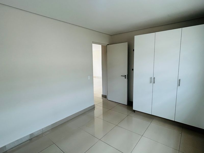 A bright, empty bedroom featuring neutral tiled flooring and a clean, white built-in wardrobe.