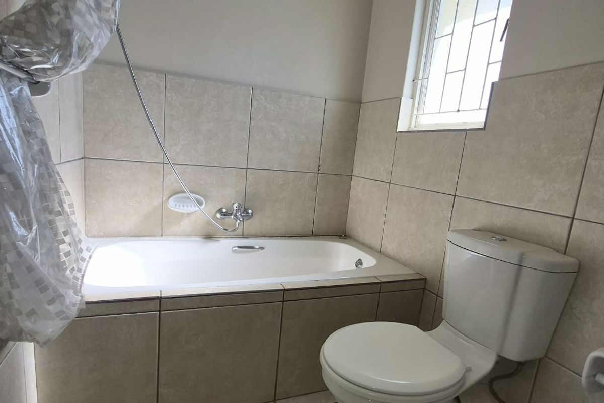 A functional bathroom featuring a built-in bathtub with shower mixer, a standard toilet, and neutral wall tiling.