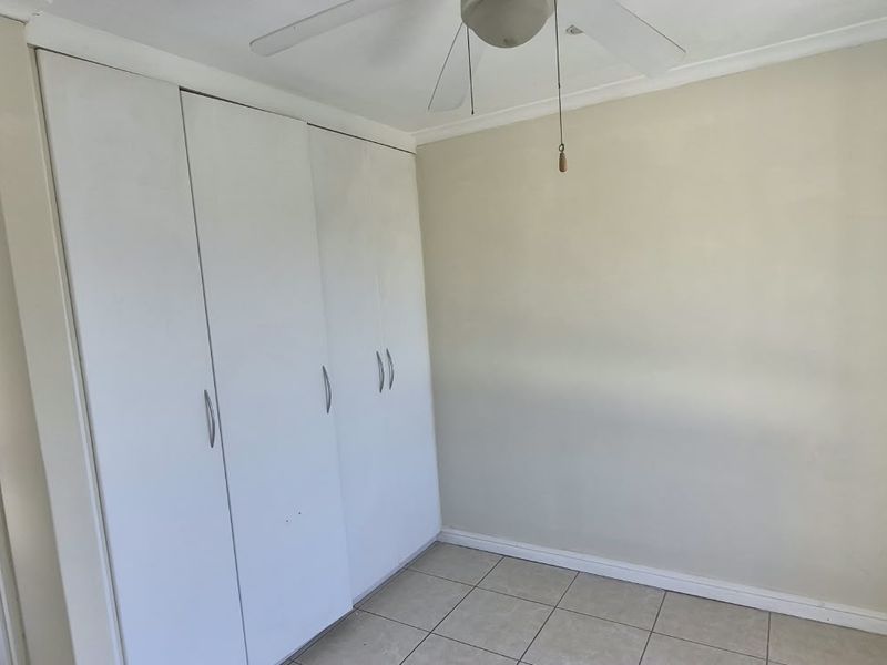 A vacant bedroom featuring tiled flooring, a ceiling fan, and built-in cupboards, offering a neutral canvas for personalization.