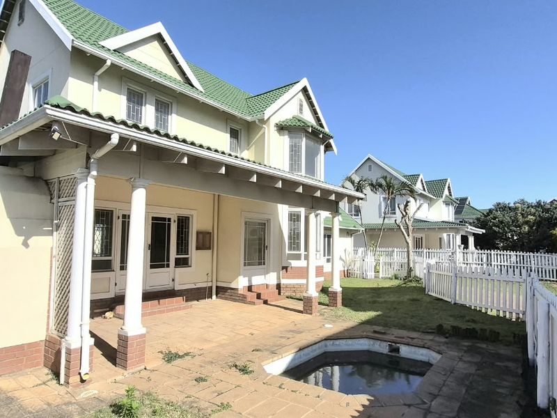 Rear view of a two-story house featuring a covered patio, a small swimming pool, and a white picket fence in a residential estate setting.