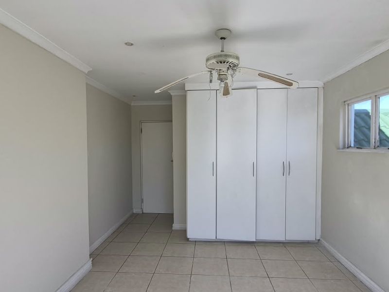 An empty bedroom featuring tiled flooring, built-in cupboards, a ceiling fan, and a wall-mounted air conditioning unit.