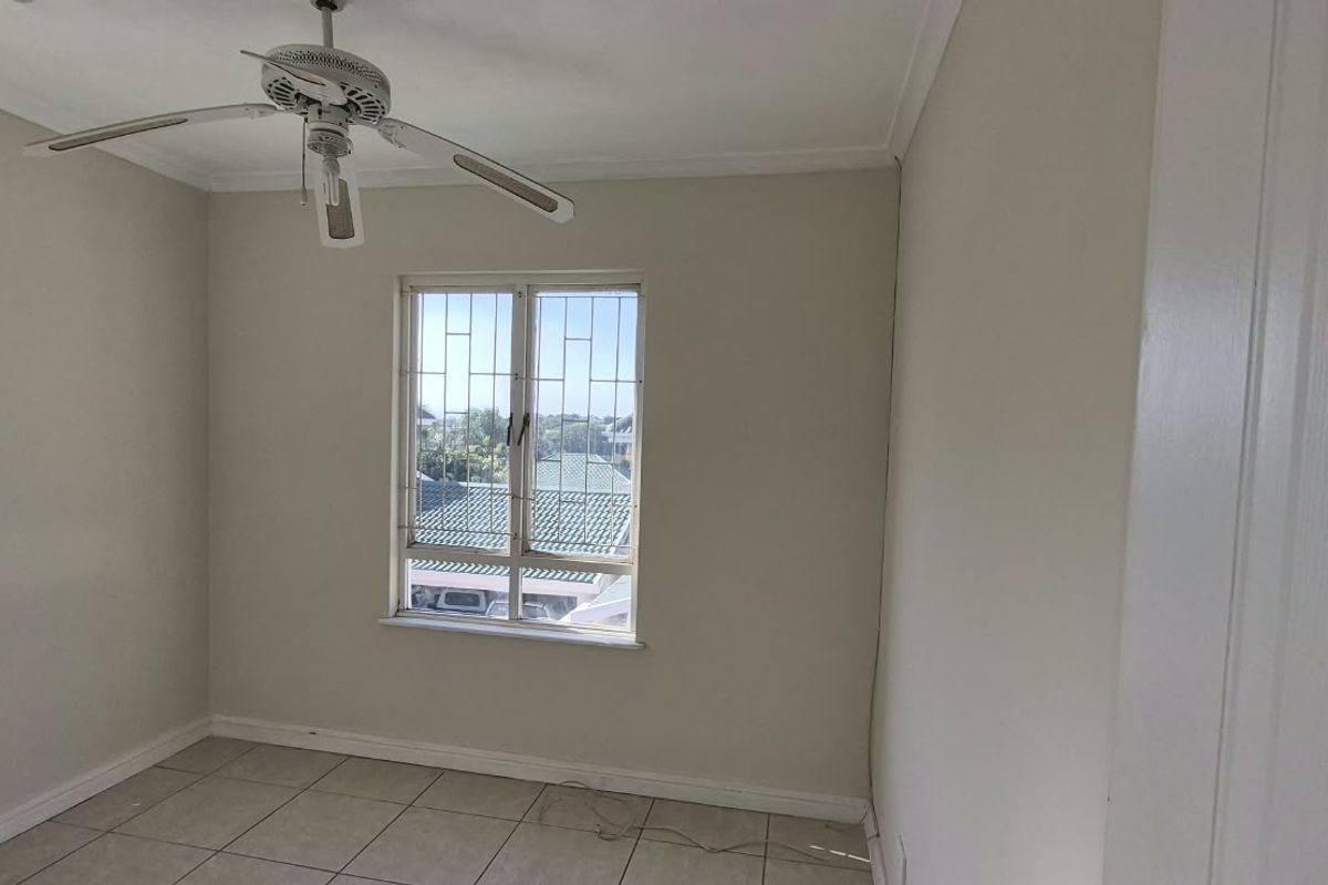 A bright, empty bedroom featuring tiled flooring, a ceiling fan, and windows fitted with security bars.