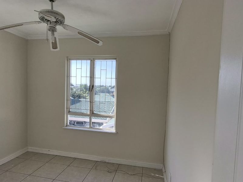A bright, empty bedroom featuring tiled flooring, a ceiling fan, and windows fitted with security bars.