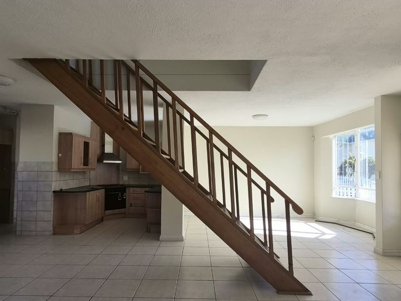 Spacious open-plan living area featuring a central wooden staircase, tiled flooring, and an integrated kitchen with built-in cabinetry.