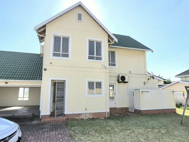 Rear view of a two-story house featuring a tiled roof, attached double garage, paved driveway, and a private garden area.
