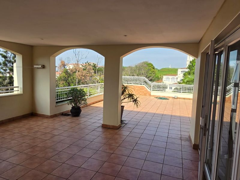 A spacious covered balcony featuring tiled flooring, arched architectural details, and metal balustrades, offering an open outdoor living area with scenic views.